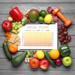 meal plan surrounded by fruits, vegetables, crackers, peanuts, a dumbell and a tape measure.