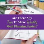 Woman Standing In Front Of Refrigerator In Kitchen With Notebook Writing Weekly Meal Plan