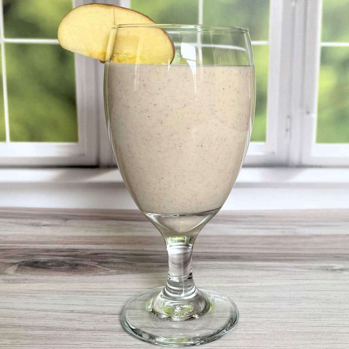 applesauce smoothie in a clear ice team glass with a apple slice garnish.