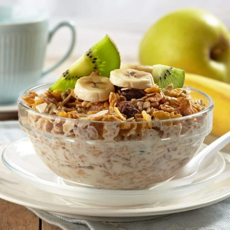 A bowl of Cereal with slices of Kiwi and banana.