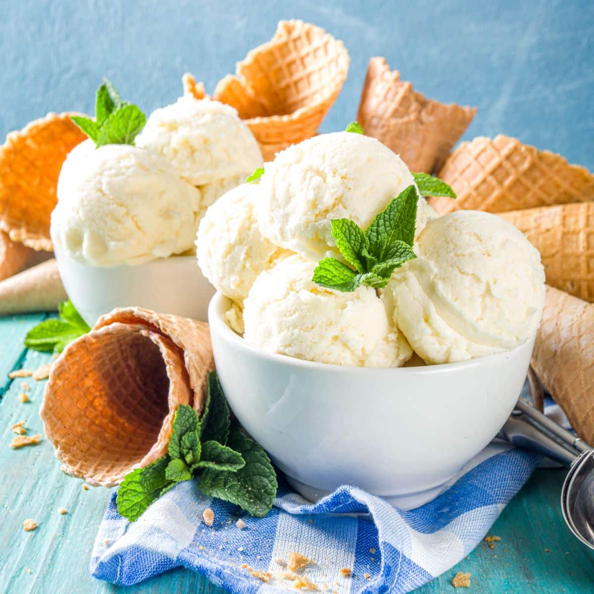 Ice cream in white bowl with mint on the top and waffle cone.