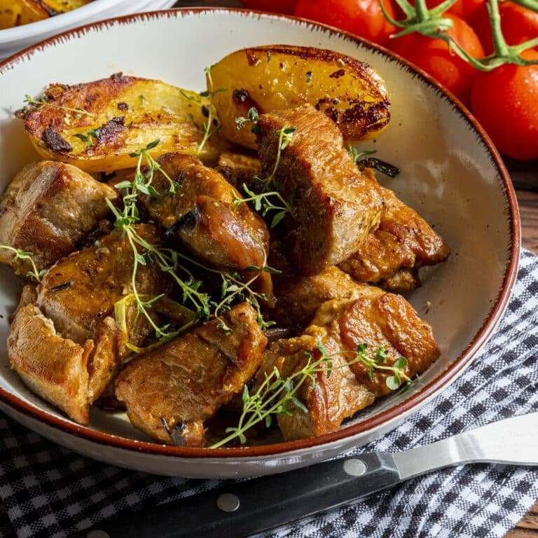 pork and potatoes in a bowl with herbs.