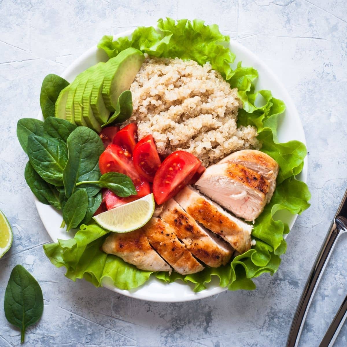 Sliced avocado, Letucce, Quinoa, Spinach, Tomatoes and Grilled Chi ken in White plate.