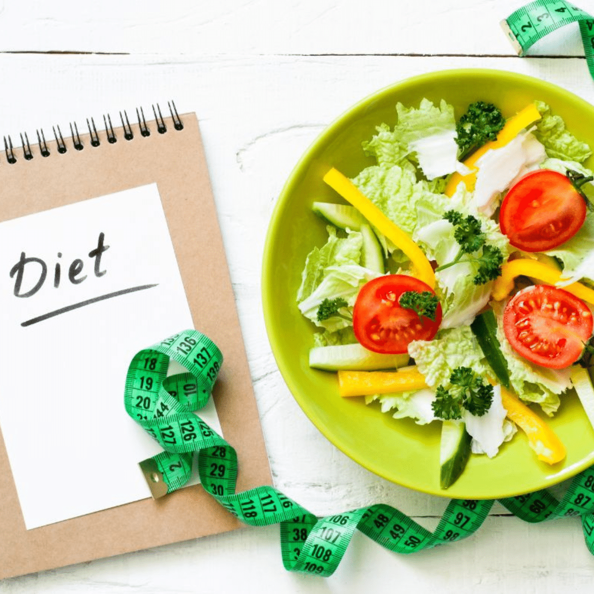 A book with Diet written on the front, green plate with vegetables salads, a fork and knife with green measuring tape