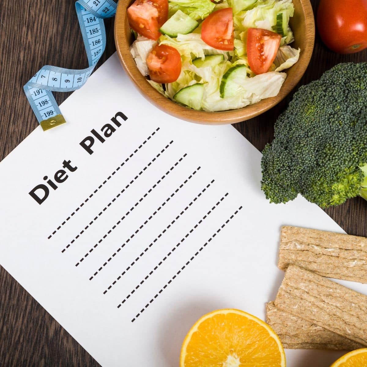 Food and sheet of paper with a diet plan on a dark wooden table.