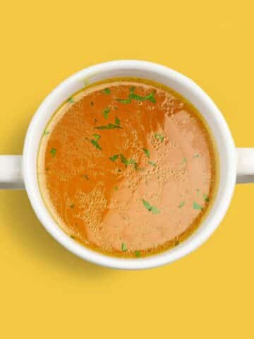Bowl of fresh chicken broth isolated on yellow background