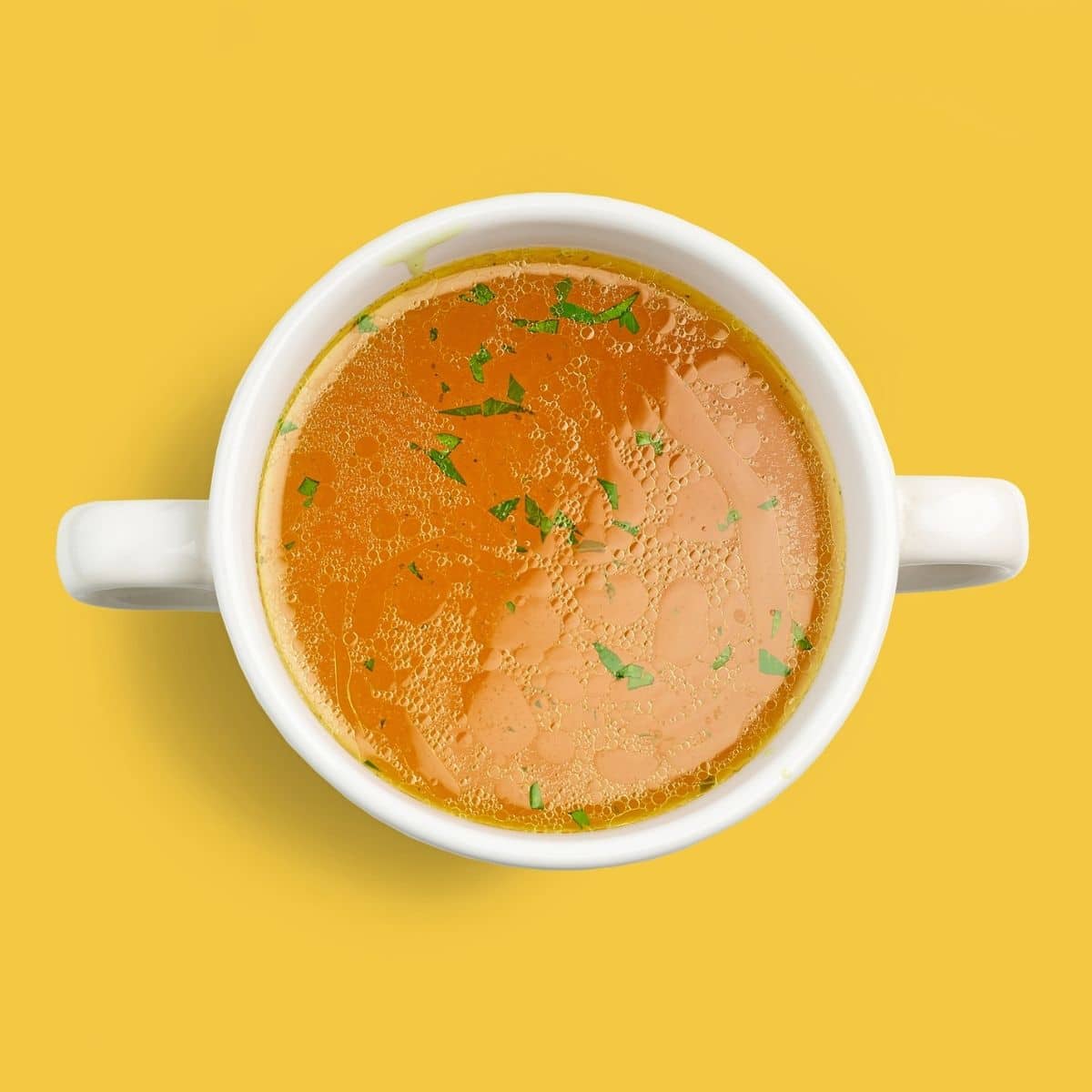 Bowl of fresh chicken broth isolated on yellow background