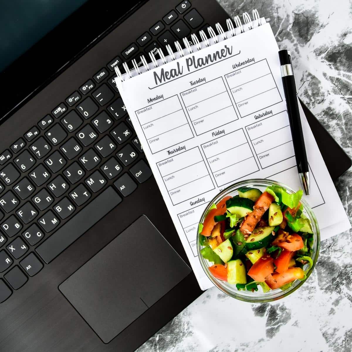 A meal plan for a week. Bowl with vegetable salad in the workplace near the computer. Lunch in the office during a break between work