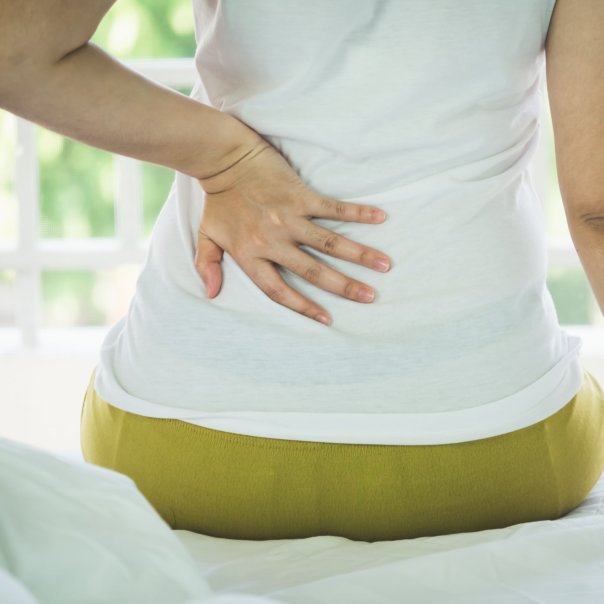 Young Woman Suffering from Pain Back While Sitting on the bed