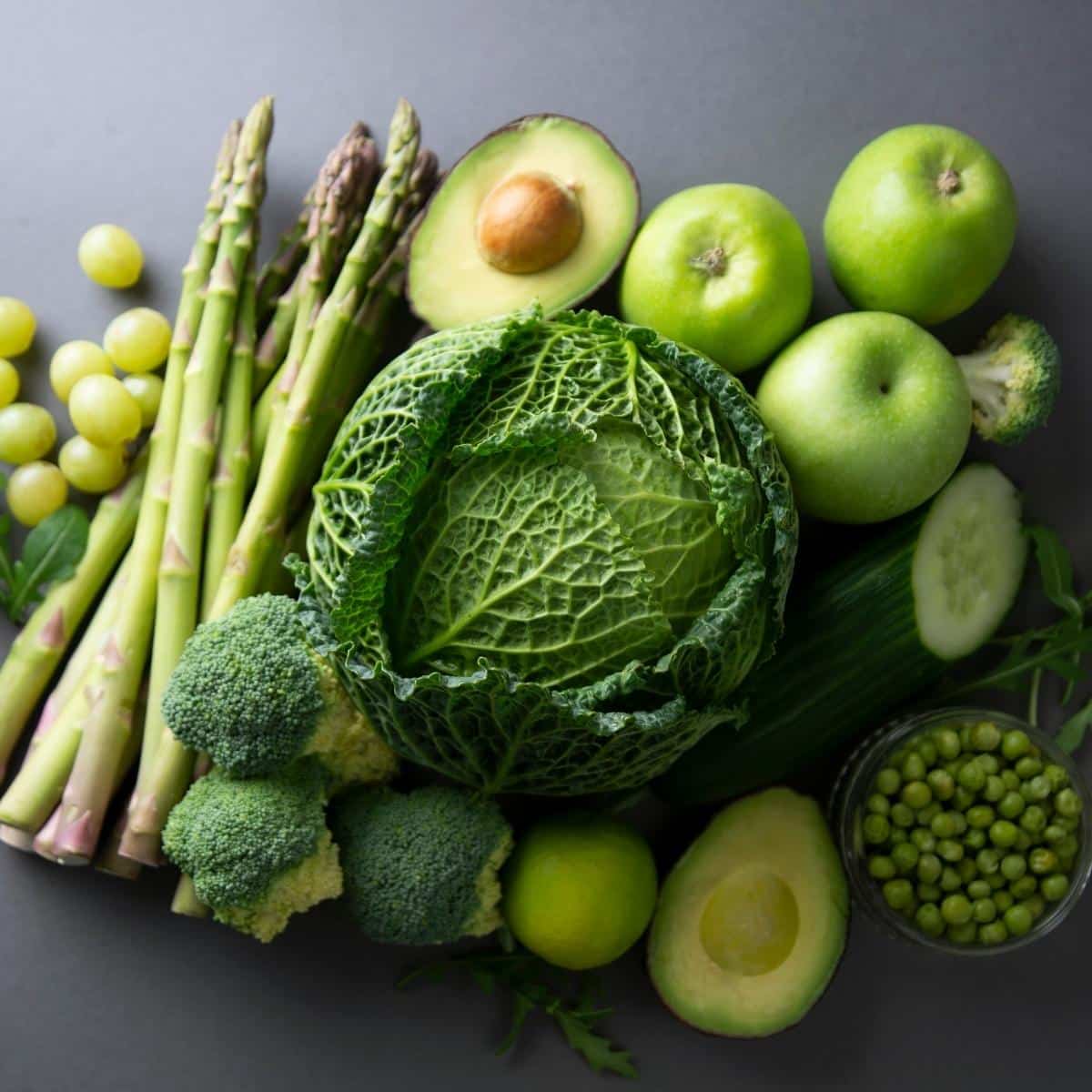 Raw healthy food clean eating vegetables: asparagus, cucumber, basil, green peas, avocado, broccoli, lime, apples, grapes, broccoli.