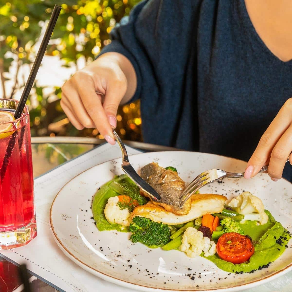 Young woman eating a fish meal with red cocktail.