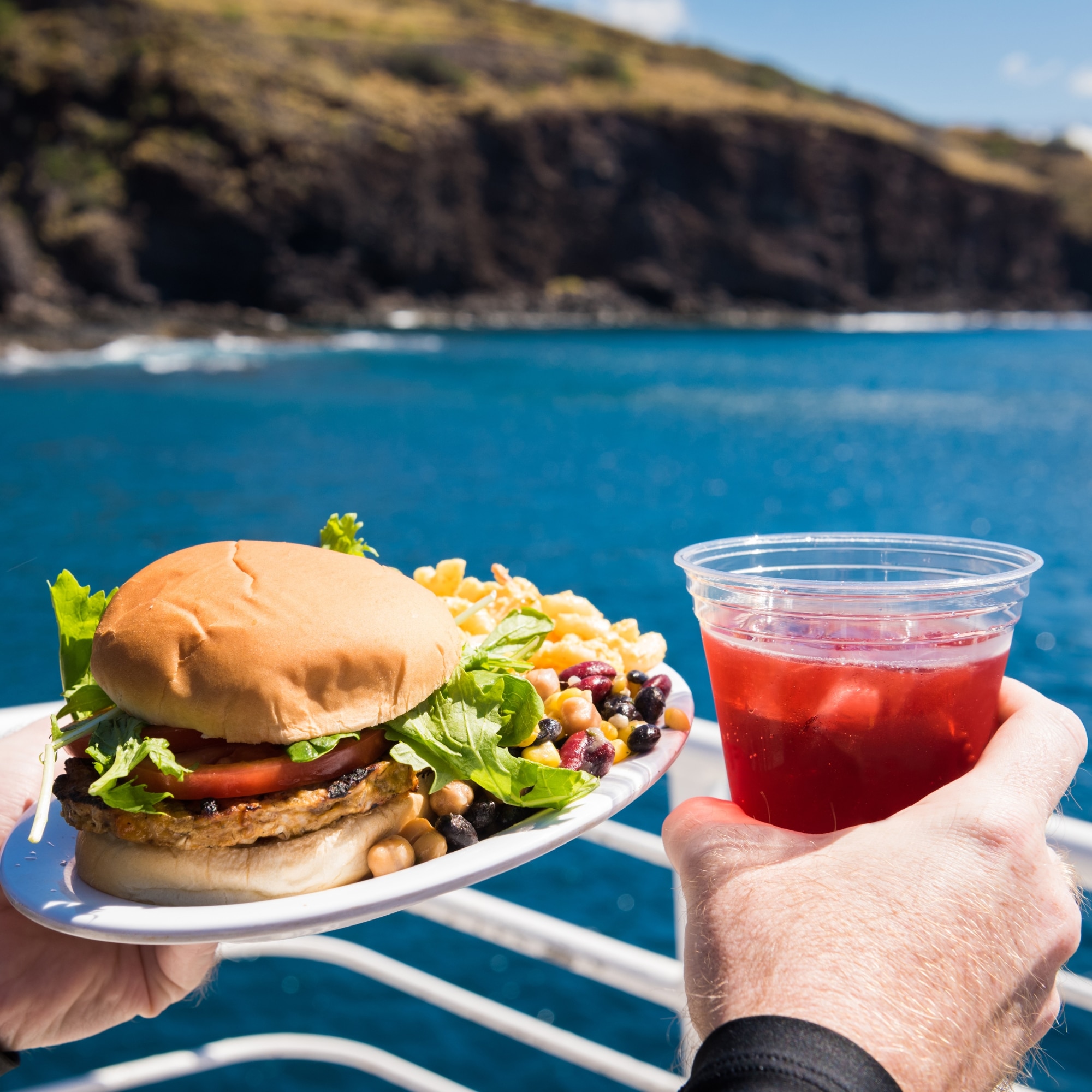 a person holding a plate with a hamburger and a drink