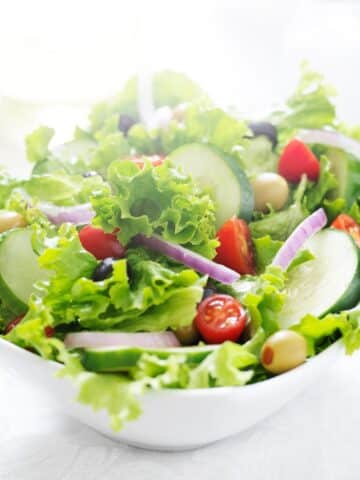 owl of Green leafy salad with olive oil, tomatoes, and cucumber.