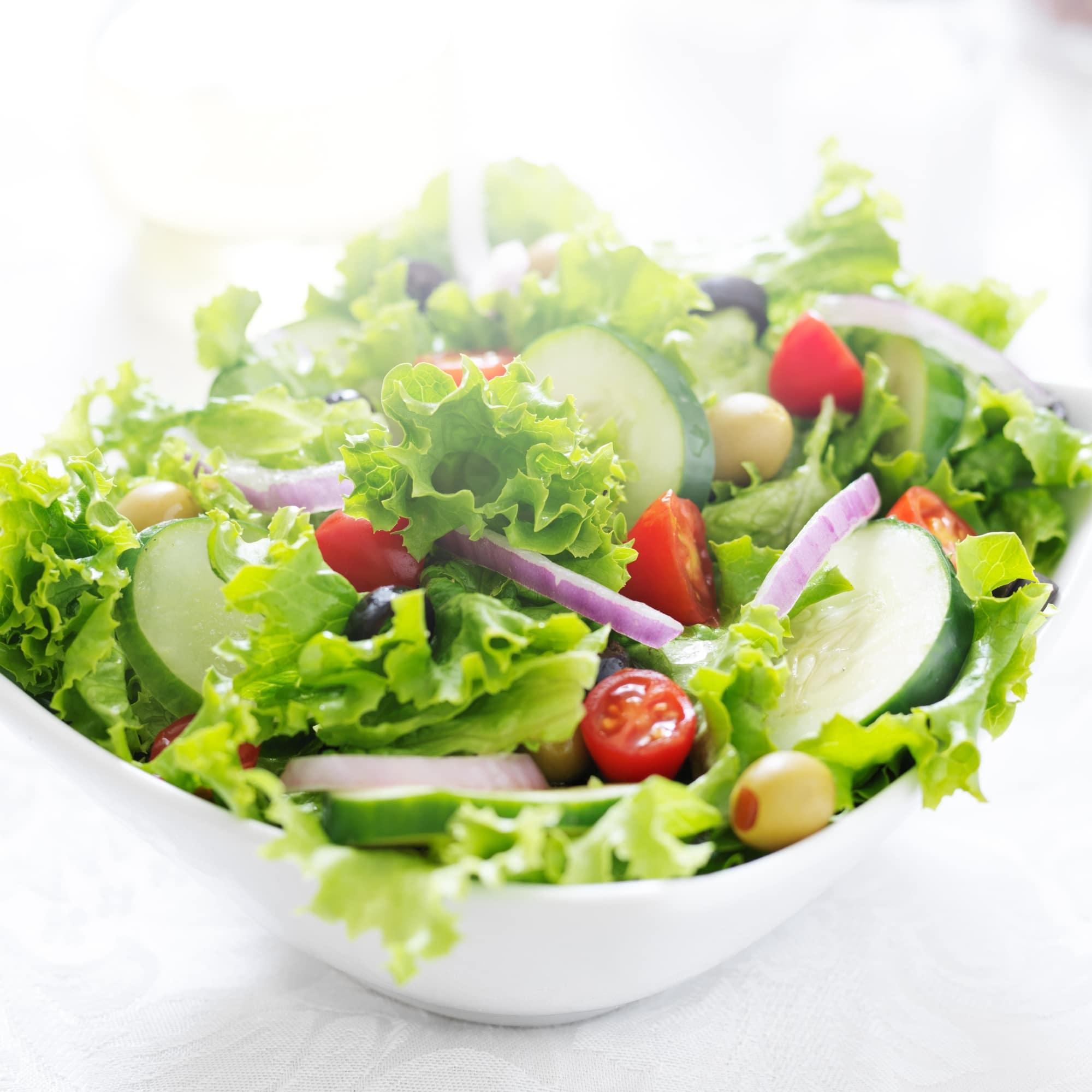 owl of Green leafy salad with olive oil, tomatoes, and cucumber.