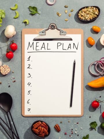meal plan on clipboard surrounded by fresh vegetables and fruits