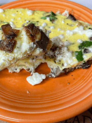 egg arugula mushroom frittata on plate with fork full close up.