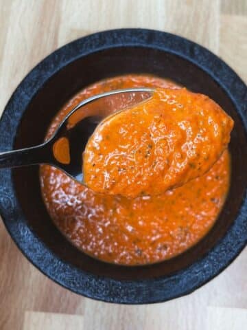 roasted red pepper sauce on a spoon in a black serving dish