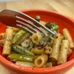 Orange bowl with fork Asparagus Pasta recipe on brown table background.