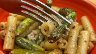 Orange bowl with fork Asparagus Pasta recipe on brown table background.