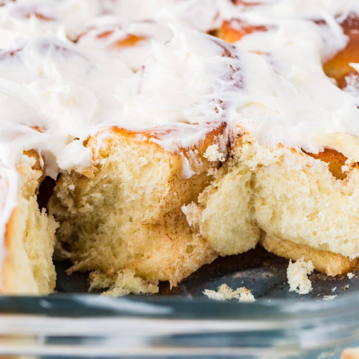 close up of flaky cinnamon rolls in a pan with icing.