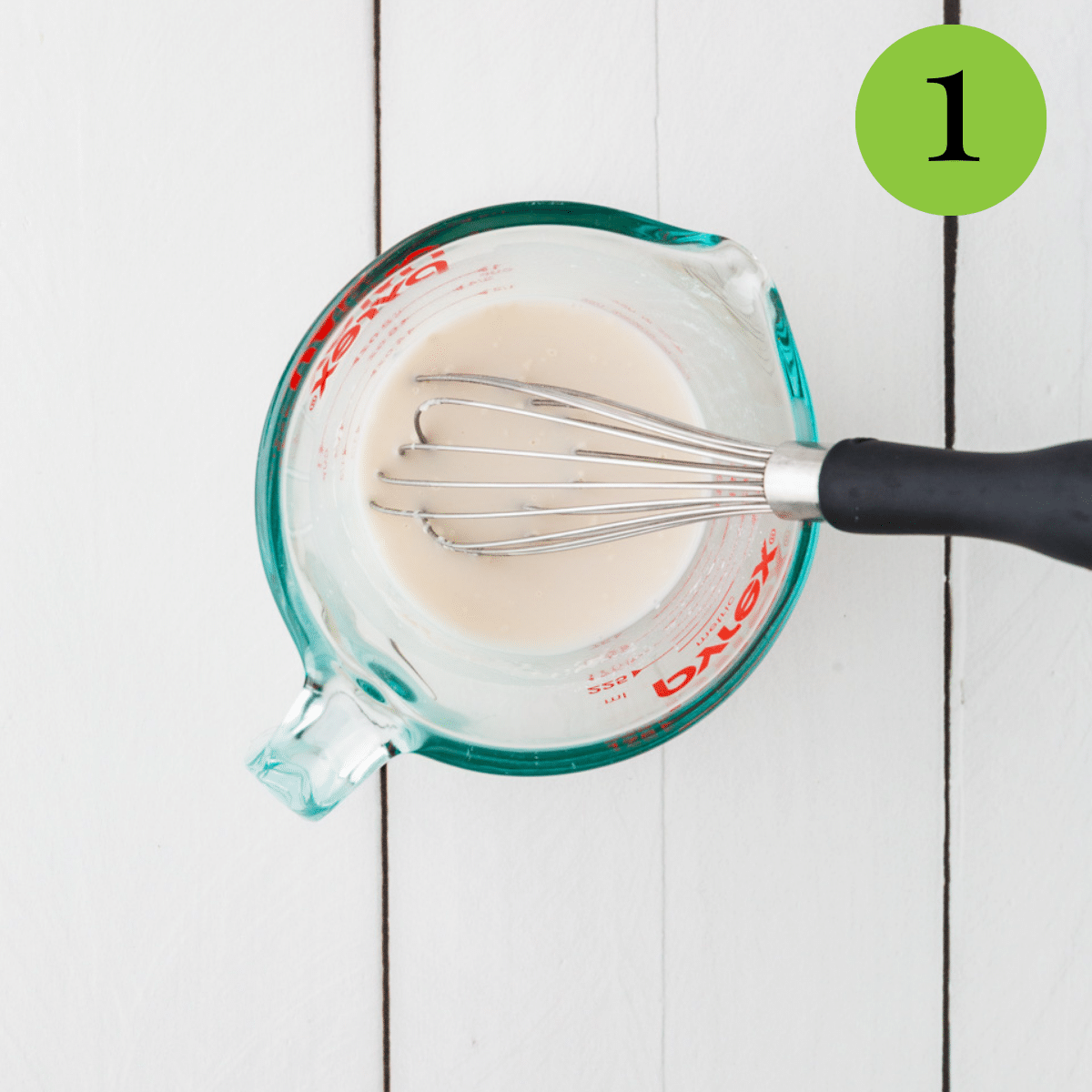 Flour and milk being added to a measuring cup as its being whisked to make skillet corn. 