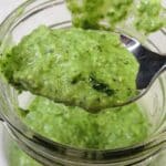 Basil pesto with lemon on a spoon being scooped up from a bowl.