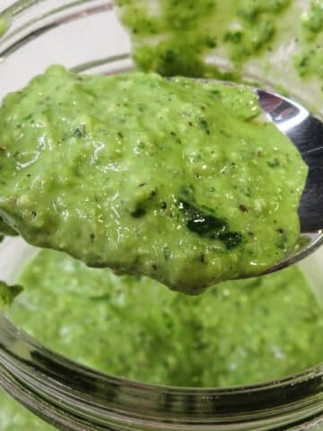 Basil pesto with lemon on a spoon being scooped up from a bowl.