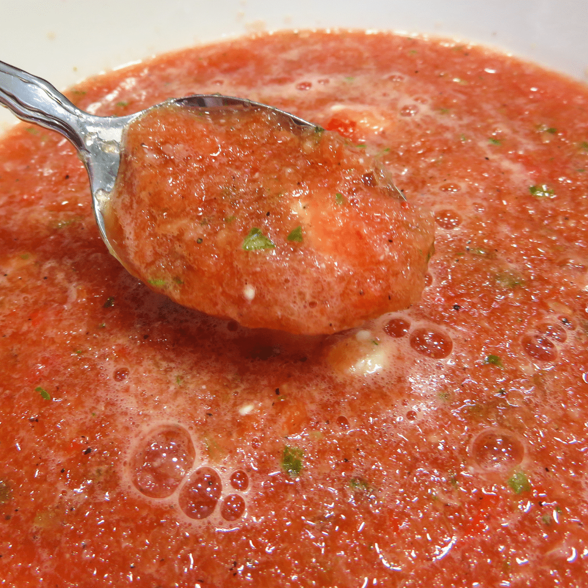 Watermelon Gazpacho in a white bowl with a metal spoon dipping in to grab a bite.