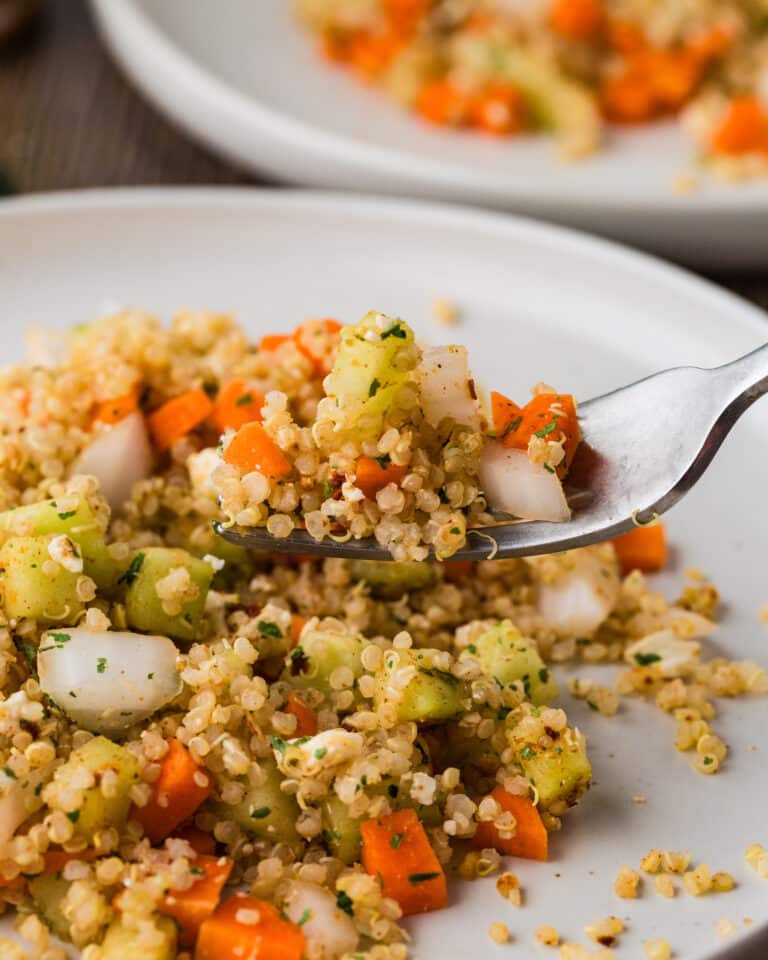 Quinoa salad on a white plate being placed on a fork to take a bite.