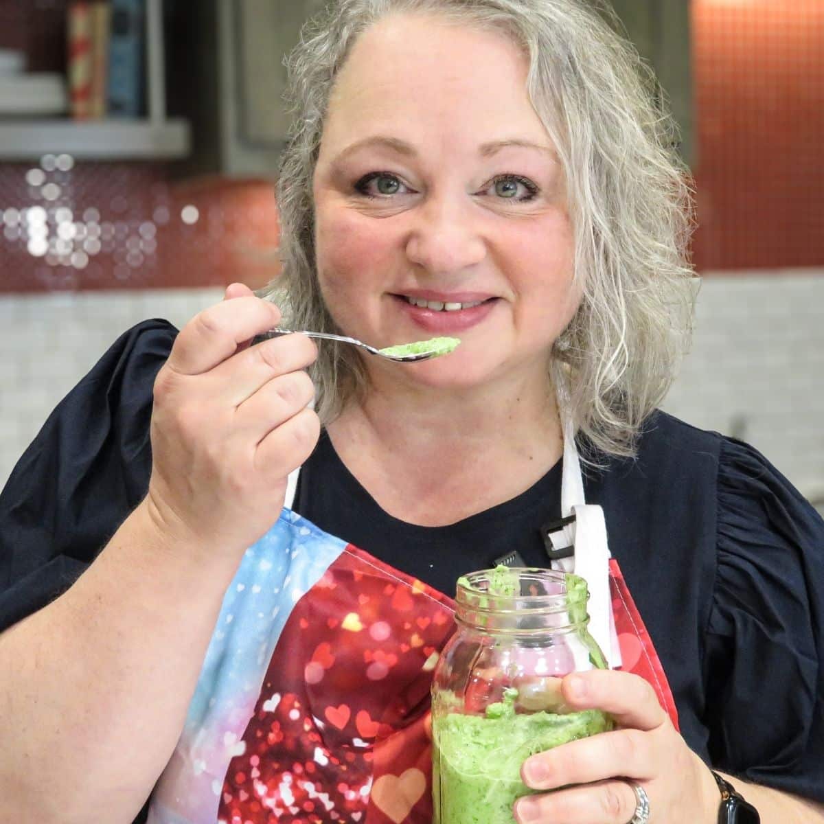 Woman with an apron enjoying a bite of pesto from a jar. 