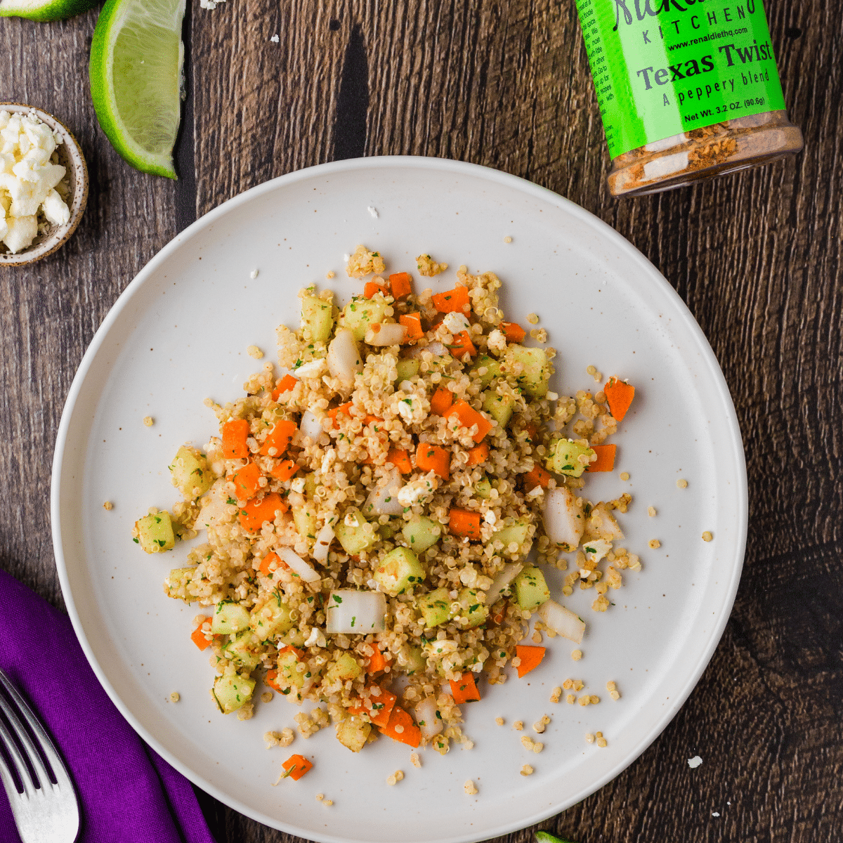 Perfectly done Quinoa salad on a white plate on a wooden table with Texas Twist seasoning in the background. 
