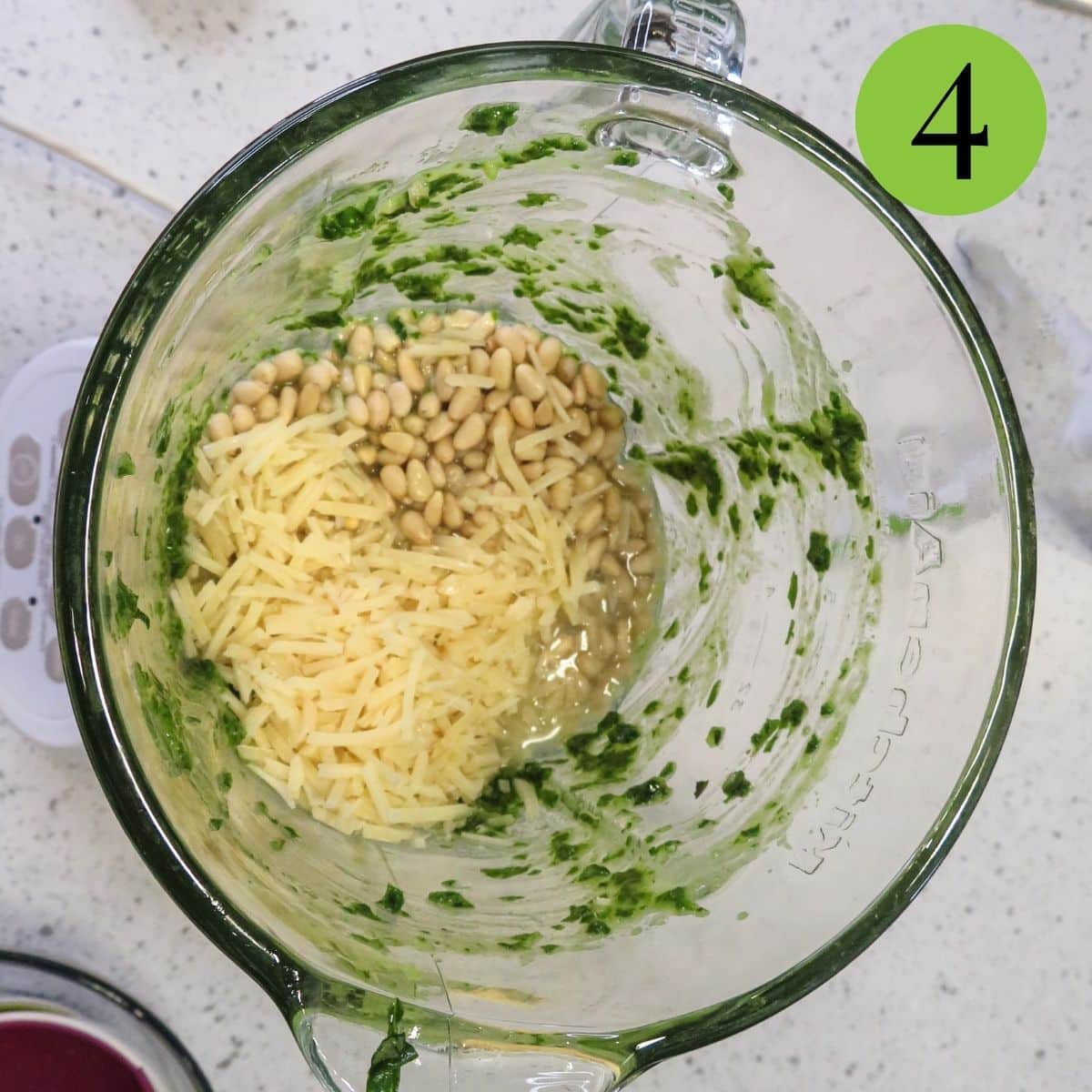 Pine nuts and parmesan cheese and lemon juice being added to the mixture in a blender. 