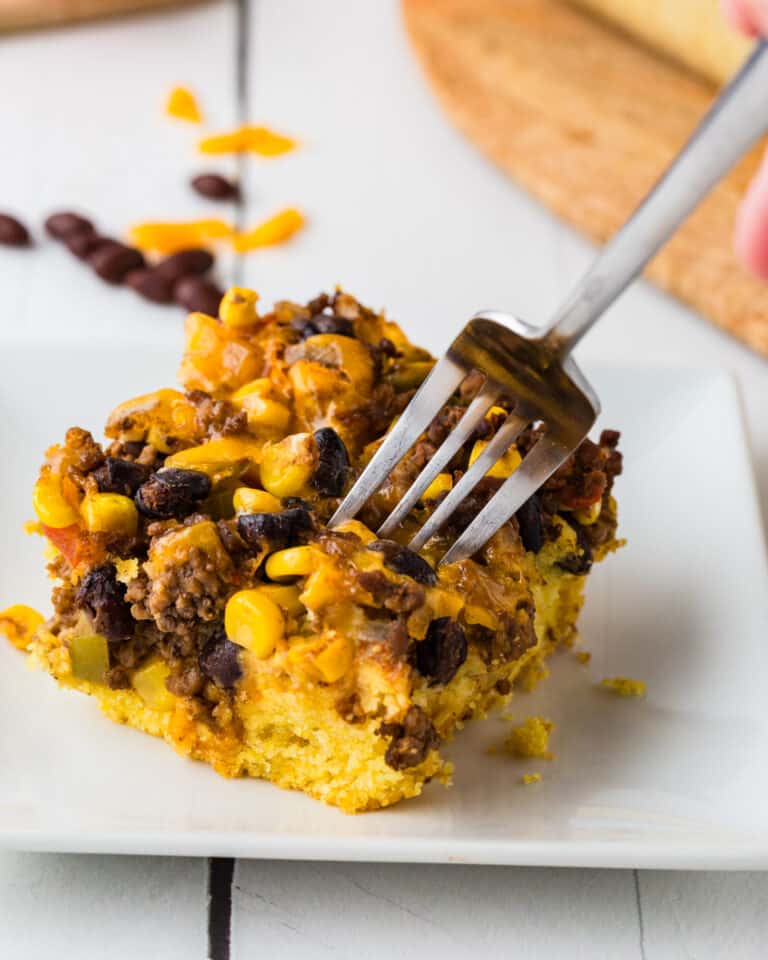 Cornbread Taco Bake on a white plate being broken apart my a metal fork to eat and enjoy.