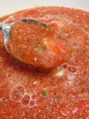 Watermelon gazpacho on a silver spoon with someone about to take a bite.