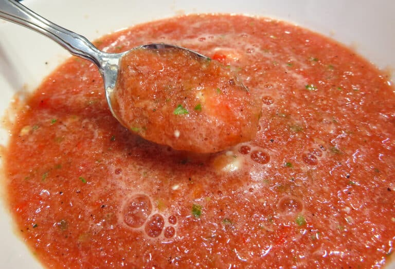 Watermelon gazpacho on a silver spoon with someone about to take a bite.