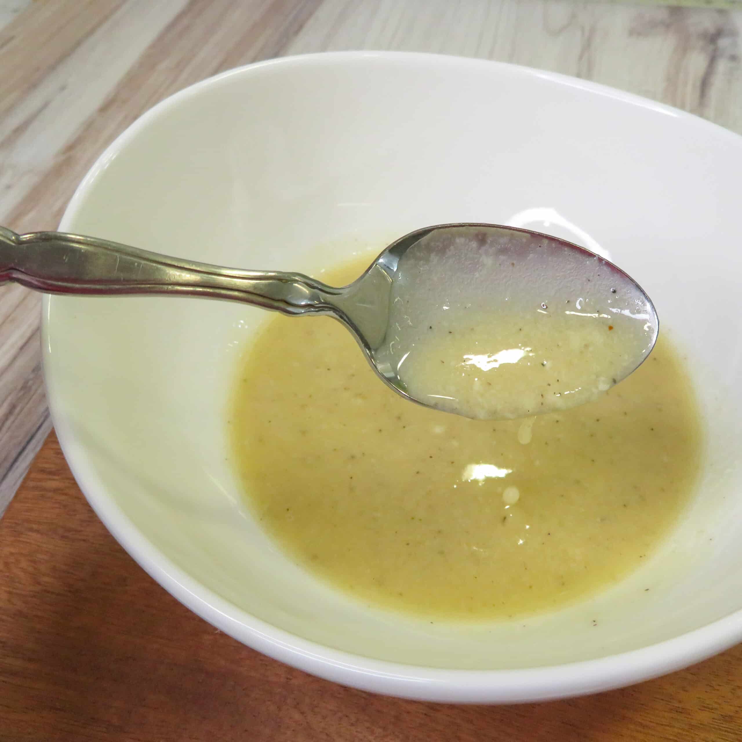 Spoon with caesar dressing with no anchovies on the spoon and in a bowl