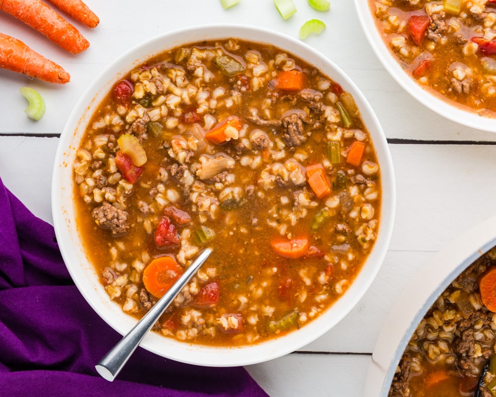Beef Barley Soup in a bowl with spoon, carrots and beef