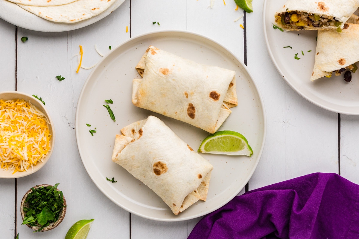 Rice, Corn and Black Bean Burritos on a plate with fixings around it