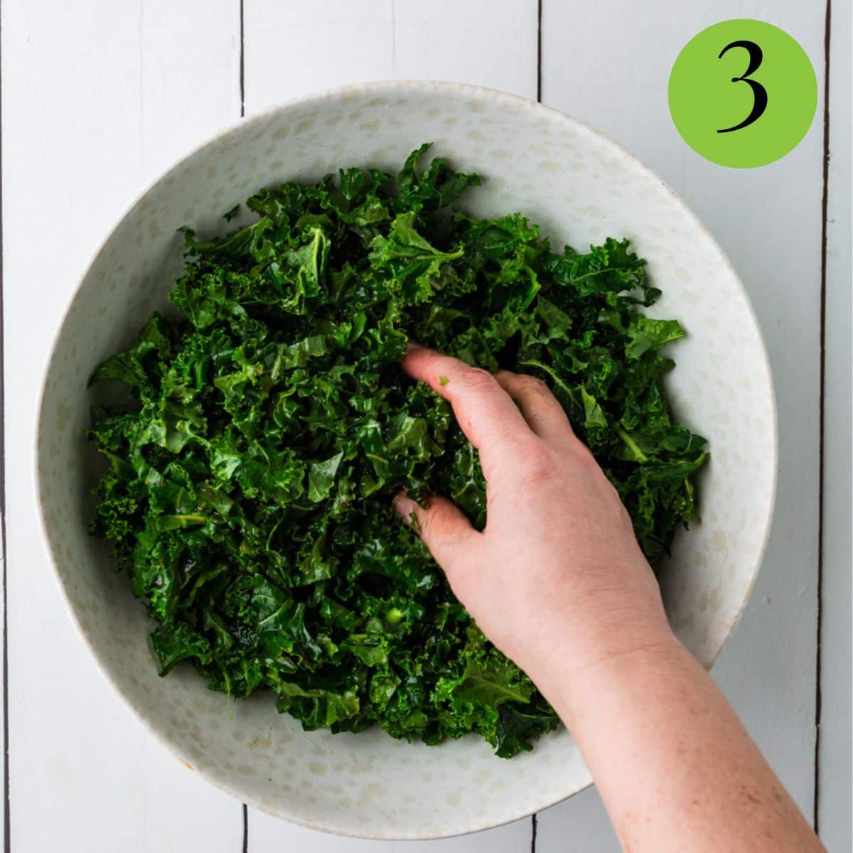 massaging the kale in the bowl with dressing